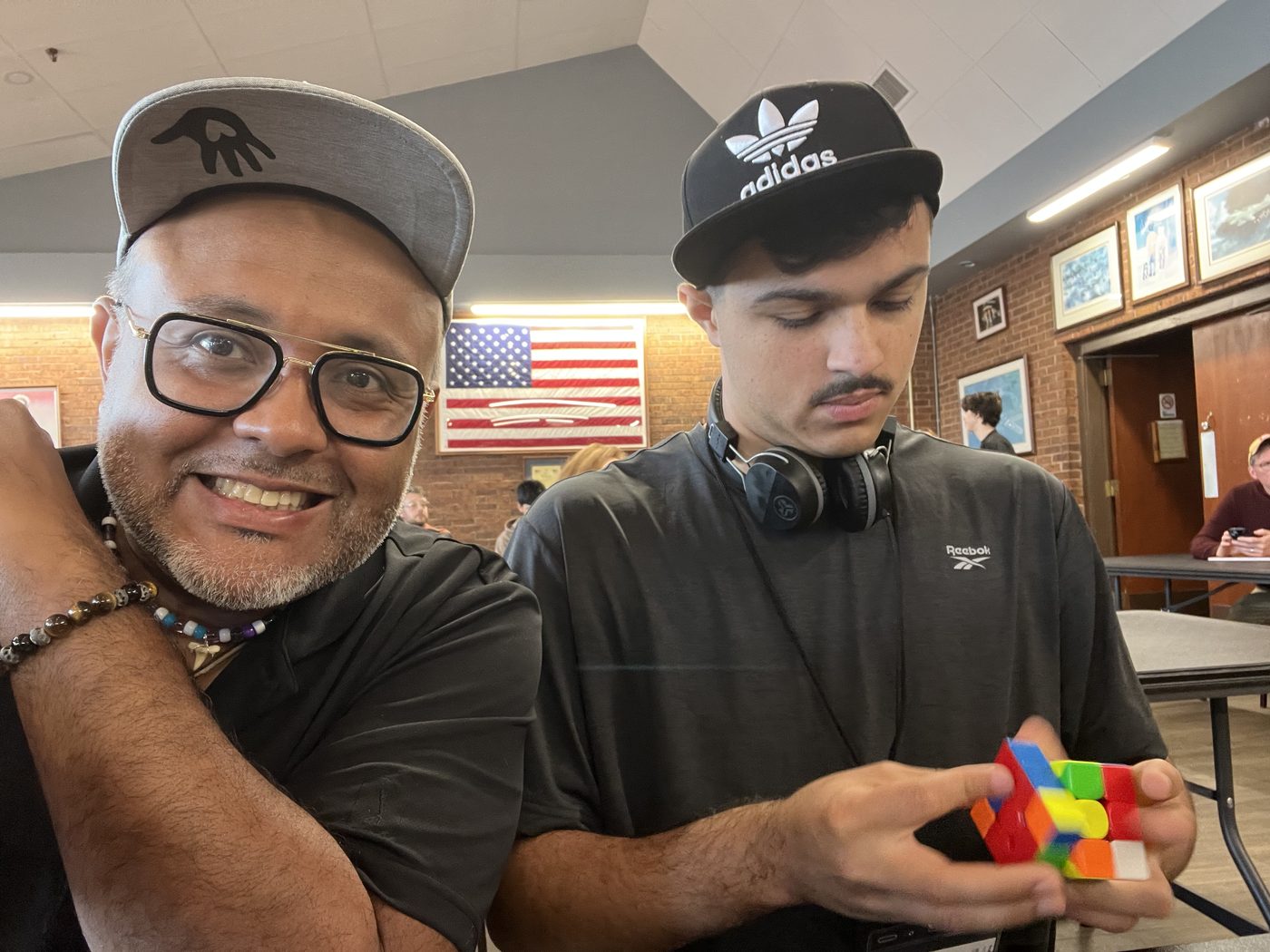 Roger Mendoza Sr. and Roger Mendoza Jr. together at a cubing competition, Roger Jr. holding a partly solved cube.